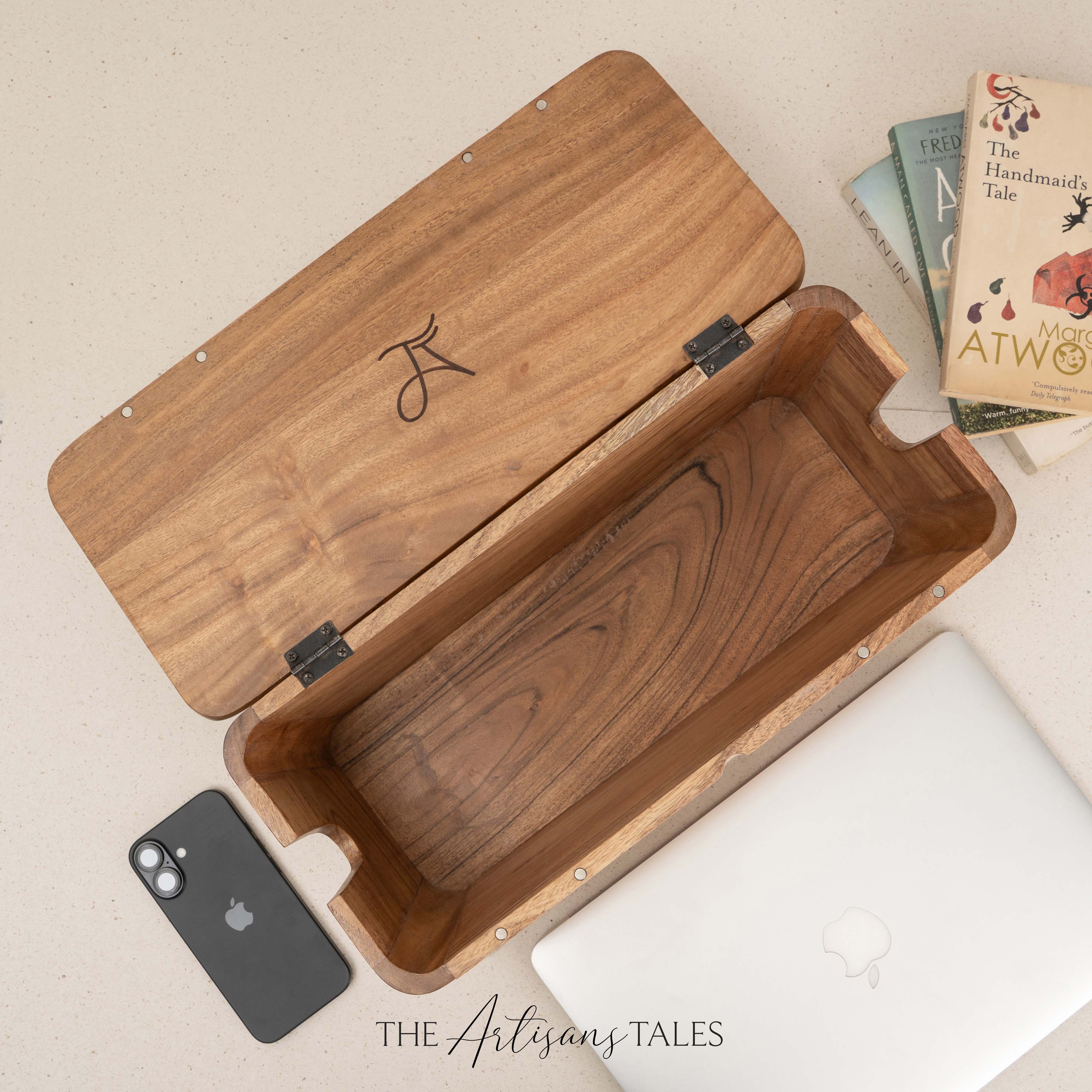 Open handcrafted wooden box with books and laptop on beige surface