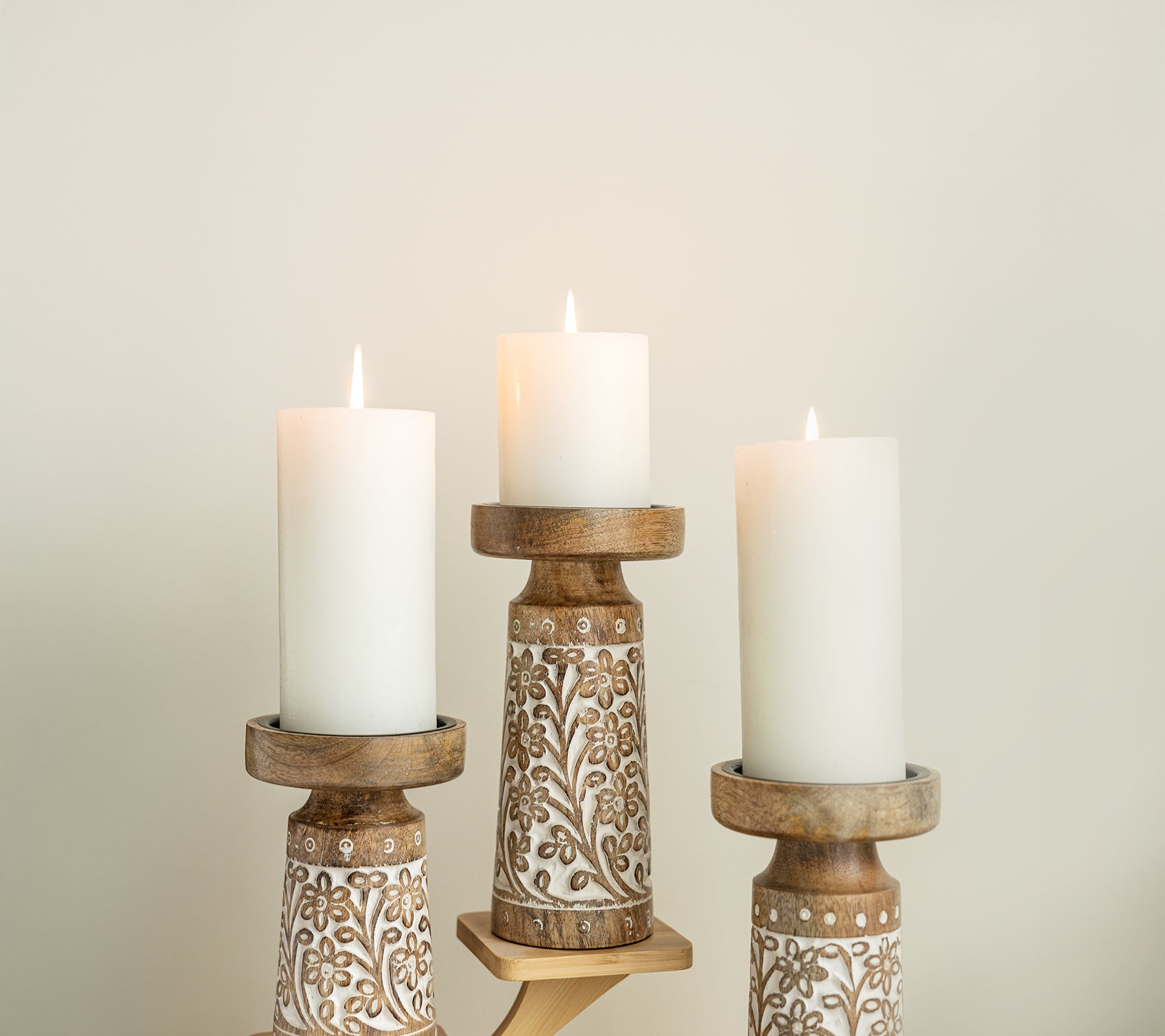 “Decorative wooden candle holders with carved floral designs holding three lit pillar candles.”