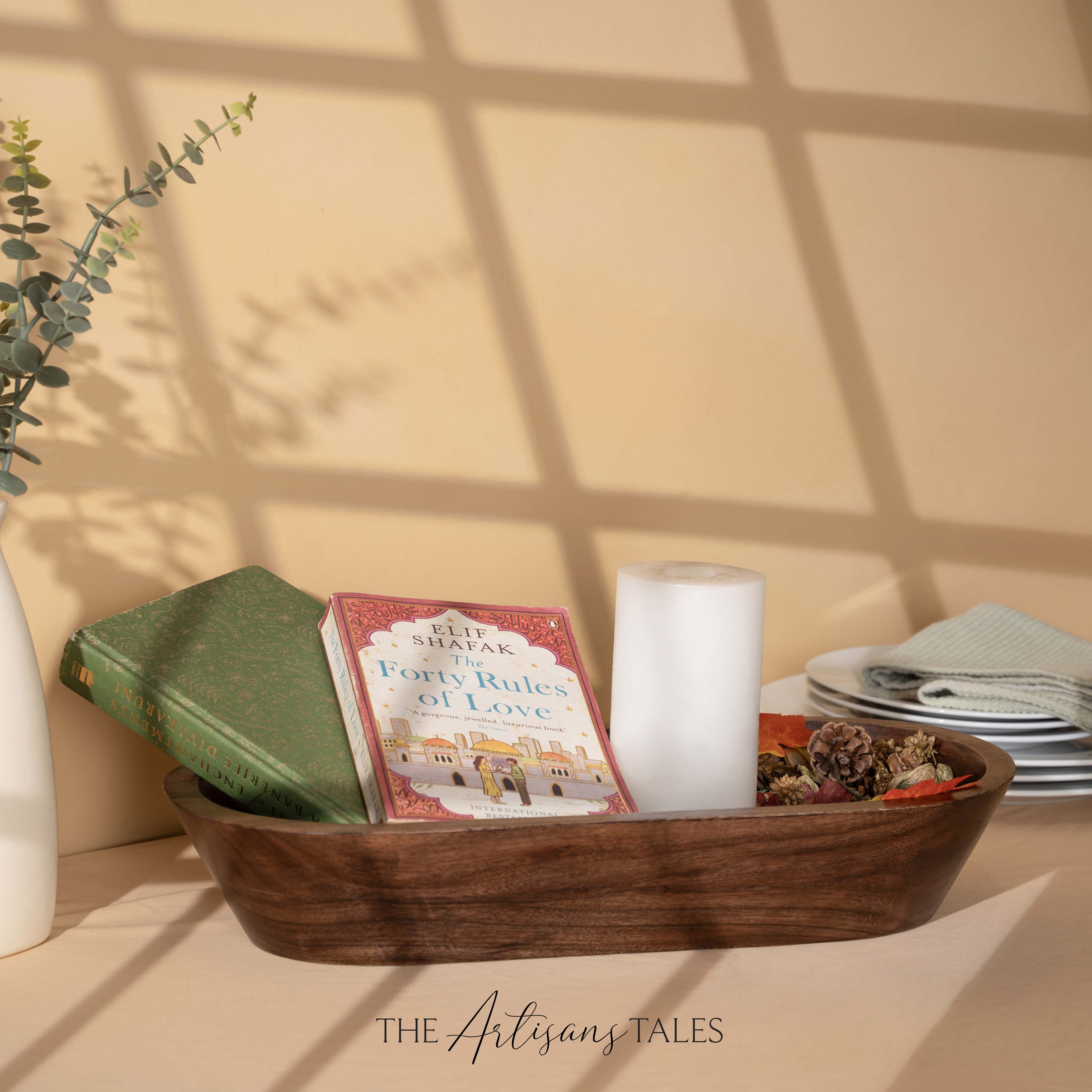 Wooden bowl with books, a candle, and decorative items on a table with a soft background.