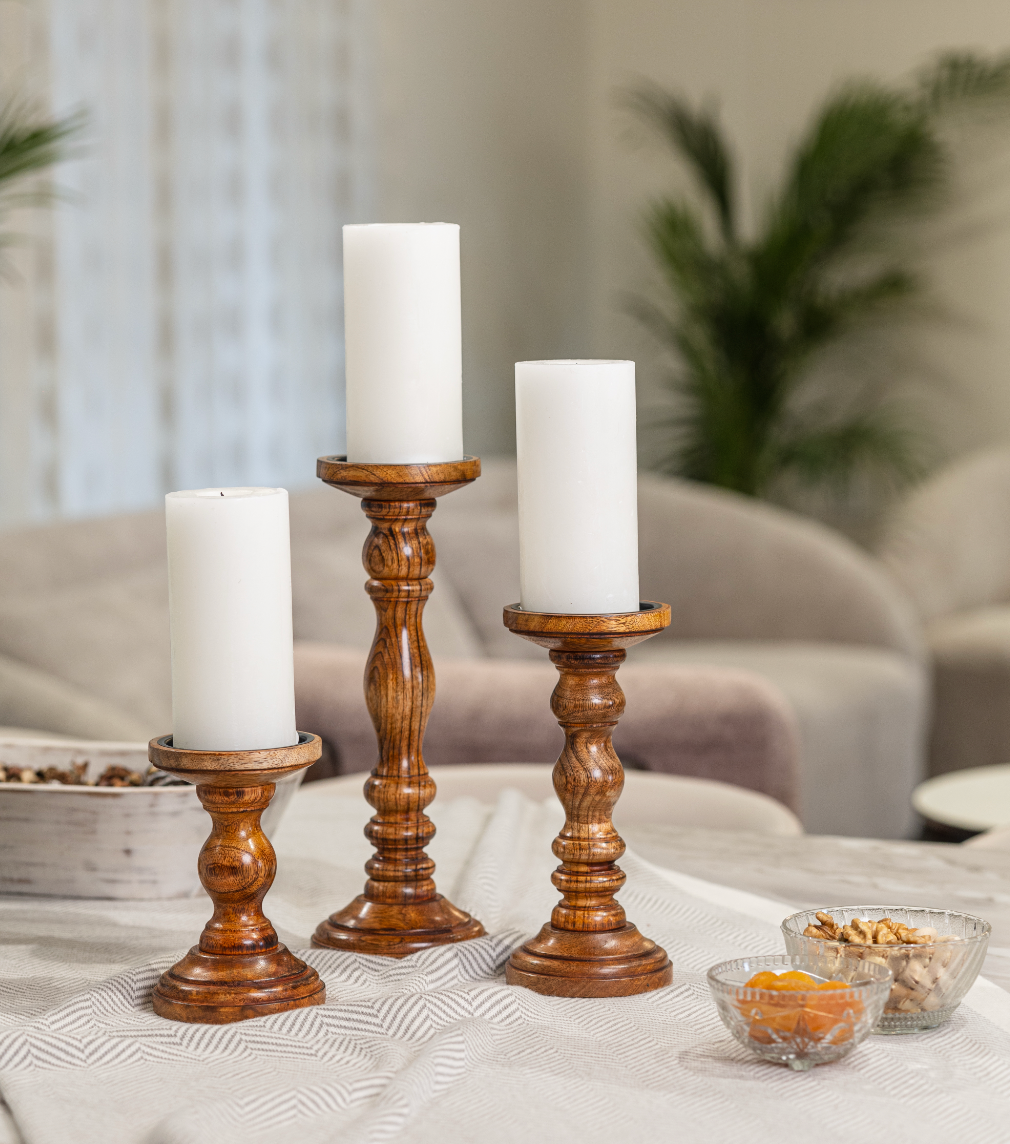 Wooden candle holders with white pillar candles arranged on a table in a cozy living room.